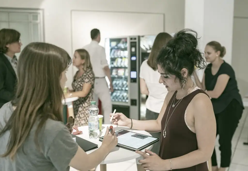 An mehreren kleinen Stehtischen sind Menschen im Gespräch vertieft.