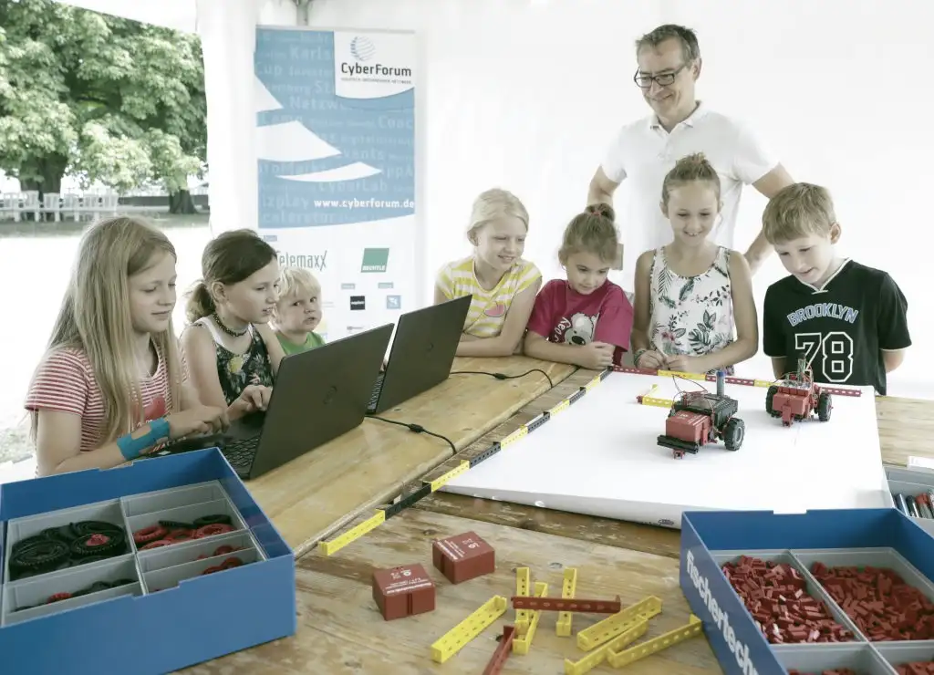 Eine Gruppe Kinder programmiert an Rechnern fischertechnik-Fahrzeuge. Bild: Jürgen Rösner