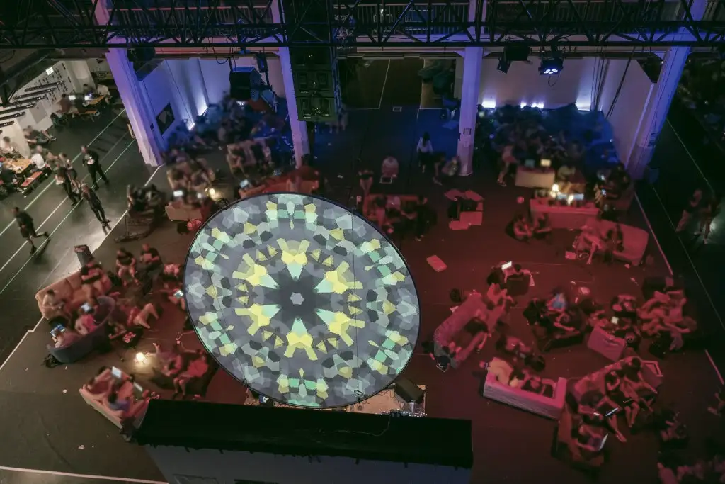 Blick auf einen großen Raum, in dem auf Sofas viele Menschen in Grüppchen sitzen. Bild von der Gulaschprogrammiernacht 2019 von @HDValentin